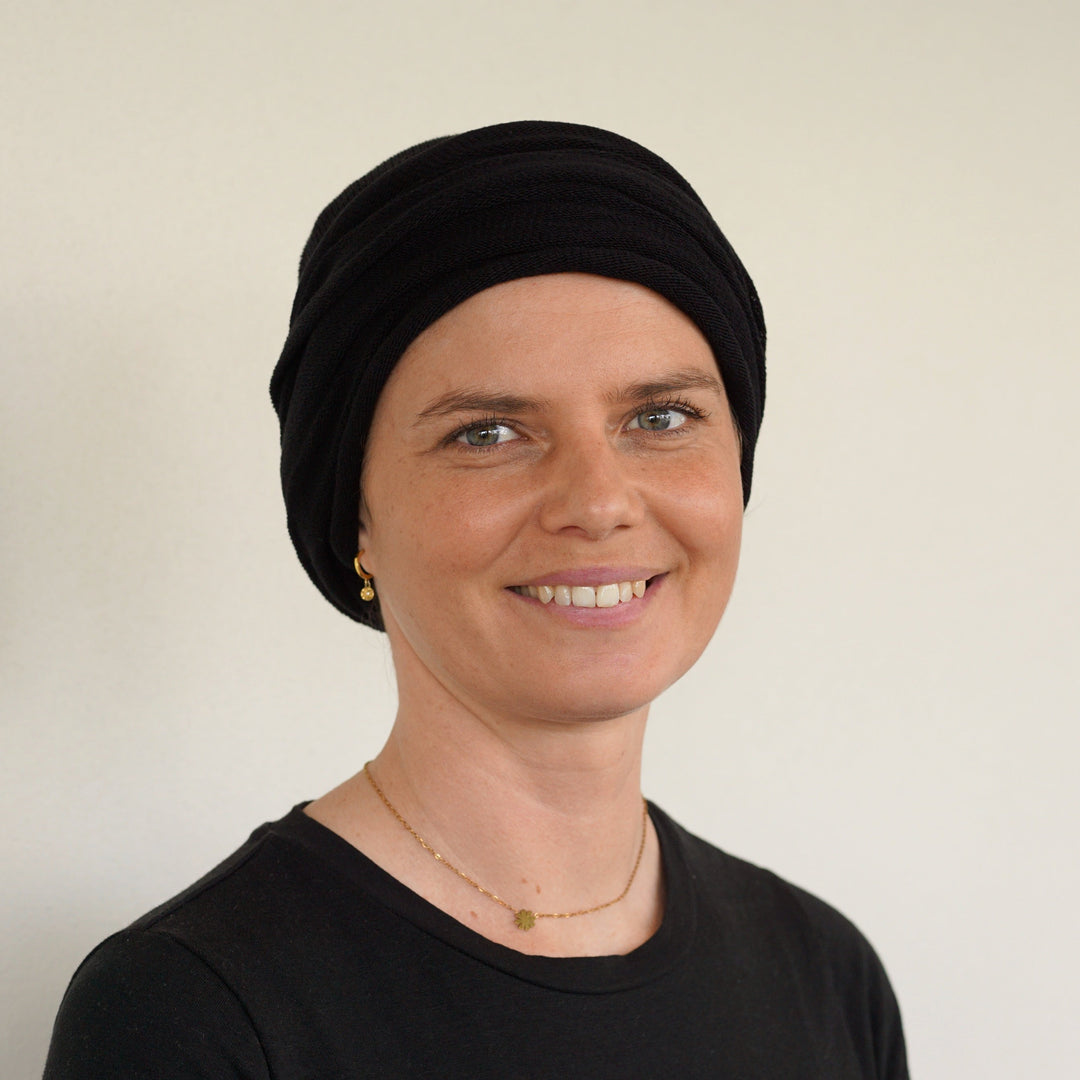 Woman wearing a black headscarf and black top against a plain background