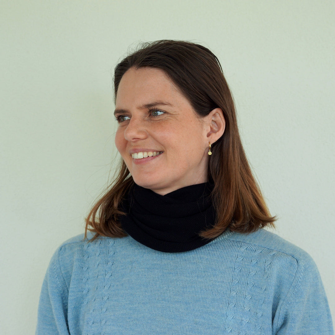 Woman wearing a blue sweater and black scarf against a light background
