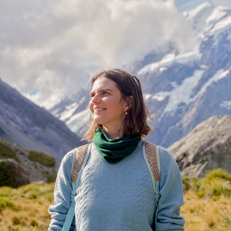 Woman standing in a mountainous landscape with snow-capped peaks.