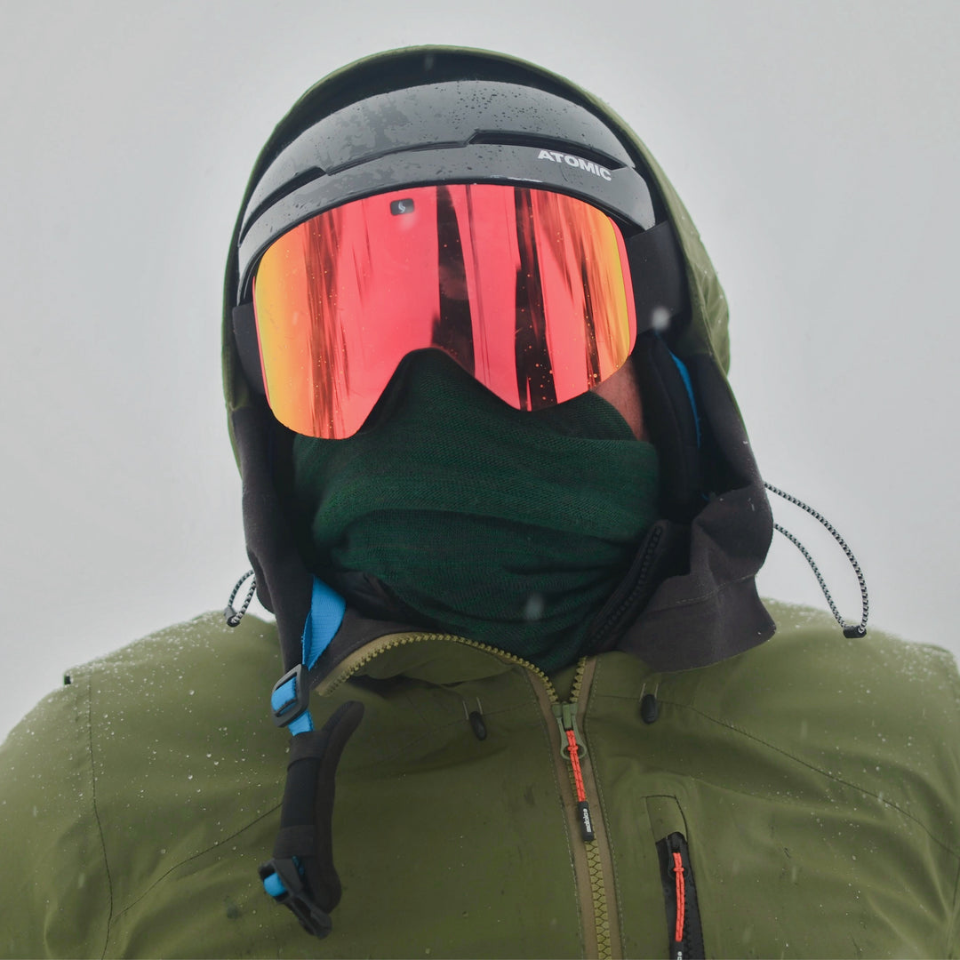 Person wearing a green jacket and black helmet with red goggles against a gray background