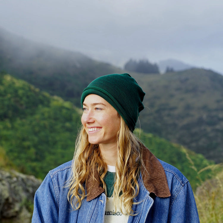 Person wearing a green beanie and blue jacket with a mountainous background