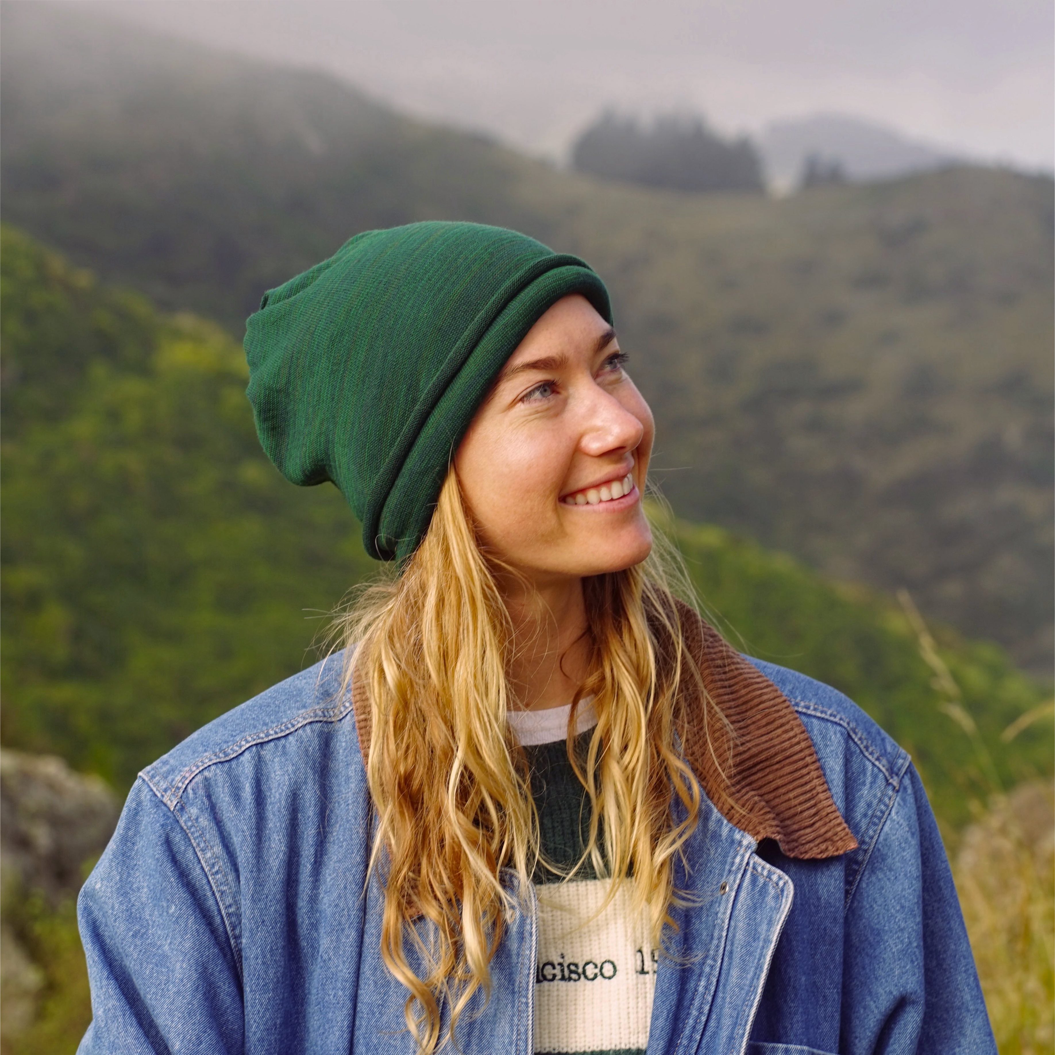 Person wearing a green beanie and denim jacket with a mountainous background